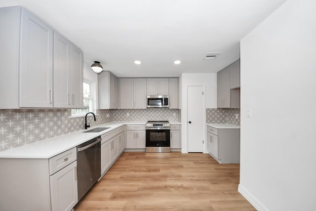 kitchen featuring light hardwood / wood-style floors, decorative backsplash, sink, gray cabinetry, and stainless steel appliances