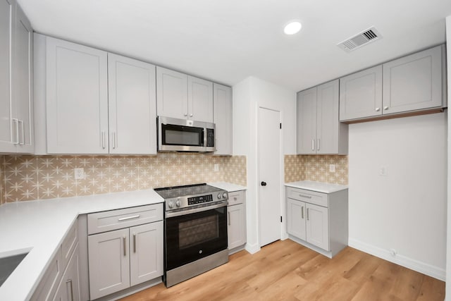 kitchen with stainless steel appliances, light hardwood / wood-style floors, and backsplash