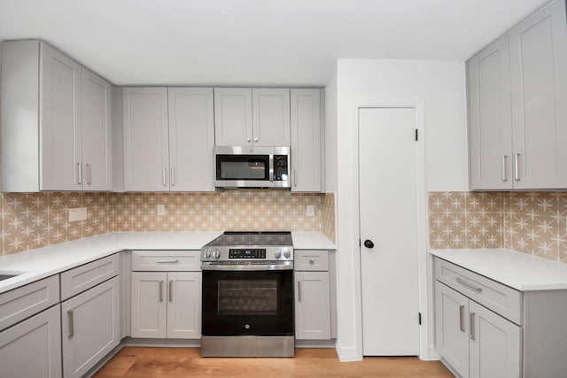 kitchen with backsplash, appliances with stainless steel finishes, gray cabinets, and light hardwood / wood-style floors