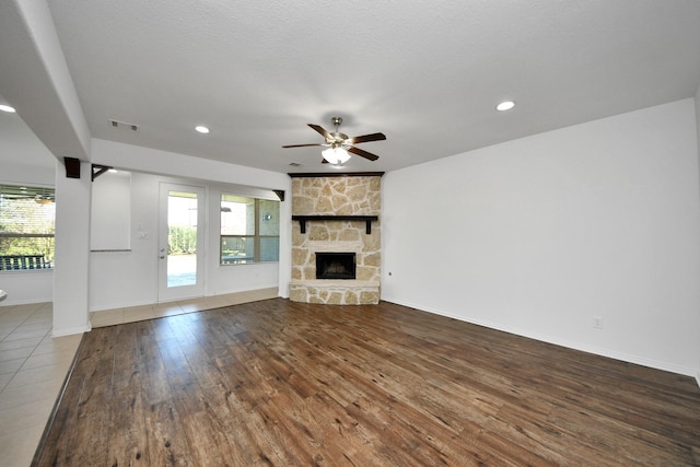 unfurnished living room featuring ceiling fan, a stone fireplace, a textured ceiling, and hardwood / wood-style flooring