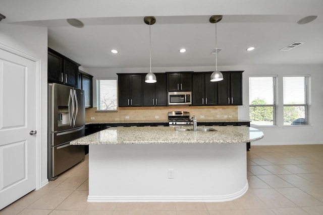 kitchen with hanging light fixtures, appliances with stainless steel finishes, light stone counters, light tile patterned flooring, and a center island with sink