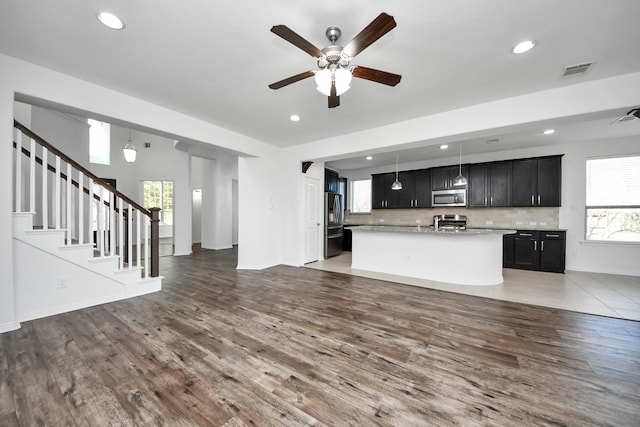 kitchen featuring pendant lighting, dark hardwood / wood-style flooring, appliances with stainless steel finishes, tasteful backsplash, and a center island with sink