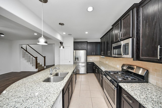 kitchen featuring light stone countertops, stainless steel appliances, tasteful backsplash, sink, and hanging light fixtures