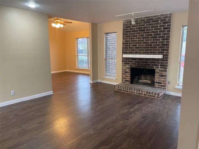 unfurnished living room featuring ceiling fan, a brick fireplace, a wealth of natural light, and track lighting