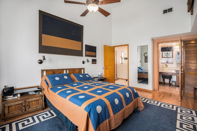 bedroom featuring ceiling fan, hardwood / wood-style floors, ensuite bath, and a towering ceiling