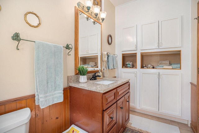 bathroom featuring toilet, tile patterned floors, wood walls, and vanity