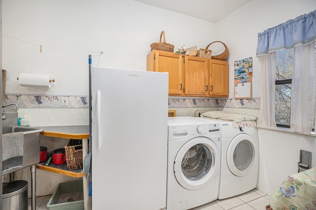 clothes washing area with light tile patterned floors, sink, washing machine and clothes dryer, and cabinets