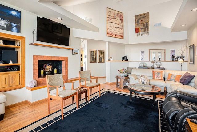 living room featuring wood-type flooring, a tile fireplace, built in features, and high vaulted ceiling