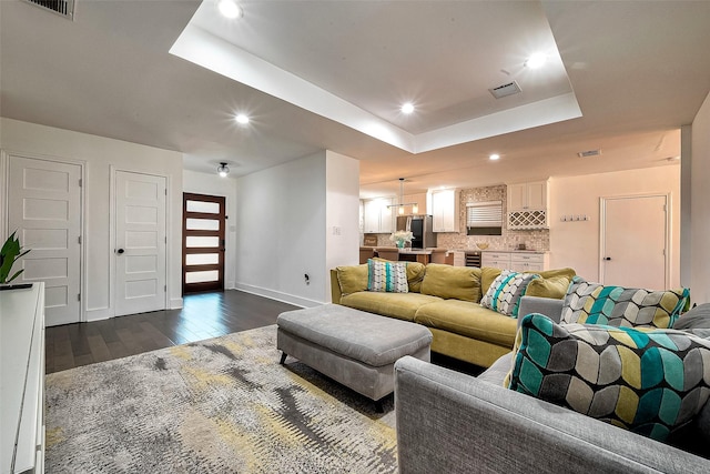 living room featuring a raised ceiling, dark wood-type flooring, and an inviting chandelier