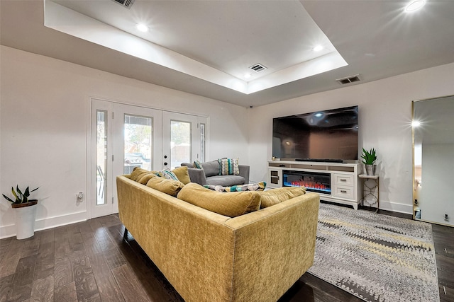 living room with dark hardwood / wood-style flooring, a raised ceiling, and french doors