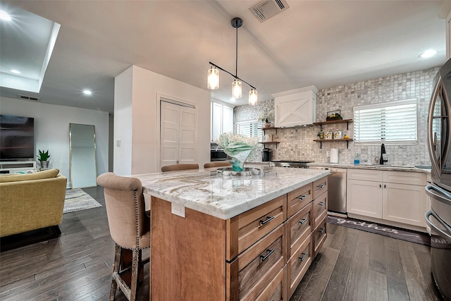 kitchen with dark hardwood / wood-style floors, a kitchen island, a kitchen bar, light stone countertops, and white cabinets