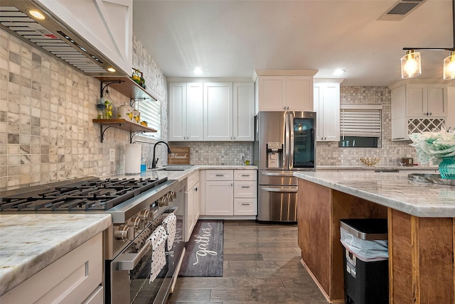 kitchen with decorative light fixtures, decorative backsplash, white cabinetry, appliances with stainless steel finishes, and light stone counters