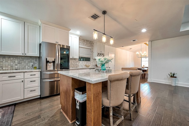 kitchen with decorative light fixtures, white cabinets, stainless steel fridge with ice dispenser, and a center island