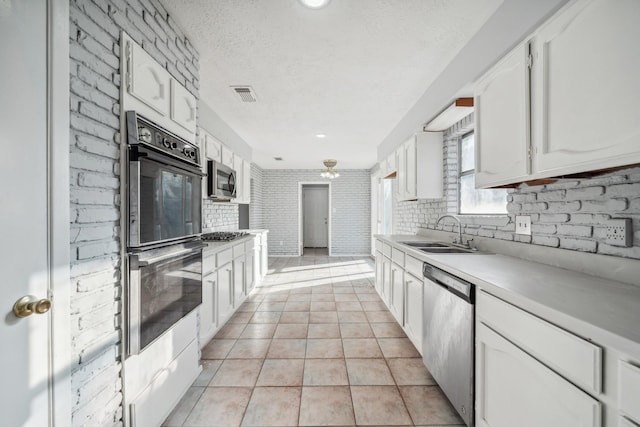 kitchen featuring sink, white cabinetry, stainless steel appliances, light tile patterned floors, and brick wall