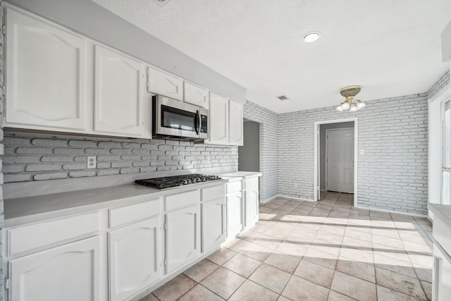 kitchen with white cabinets, brick wall, light tile patterned floors, and stainless steel appliances