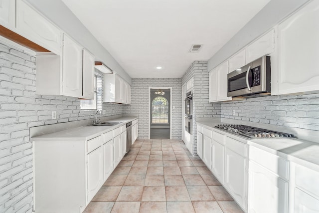 kitchen with sink, white cabinetry, stainless steel appliances, light tile patterned floors, and brick wall