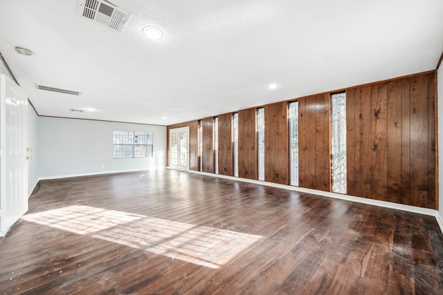 empty room with crown molding, wood walls, and hardwood / wood-style flooring