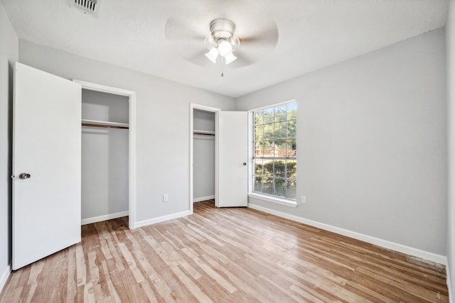 unfurnished bedroom with ceiling fan, two closets, and light hardwood / wood-style floors