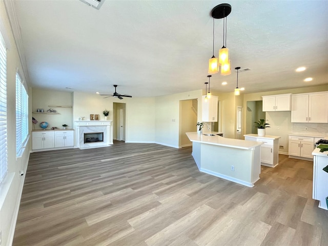 kitchen featuring white cabinetry, decorative light fixtures, a kitchen island with sink, light hardwood / wood-style floors, and backsplash