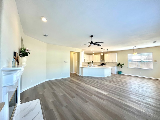 unfurnished living room featuring visible vents, baseboards, wood finished floors, and a glass covered fireplace