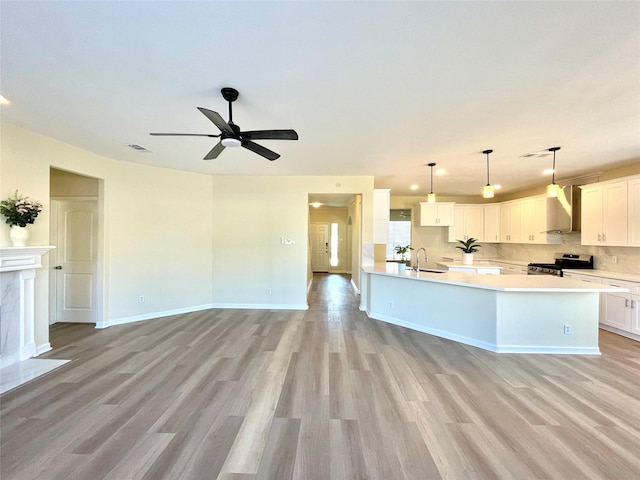 kitchen featuring a sink, open floor plan, light countertops, wall chimney range hood, and stainless steel range with electric stovetop