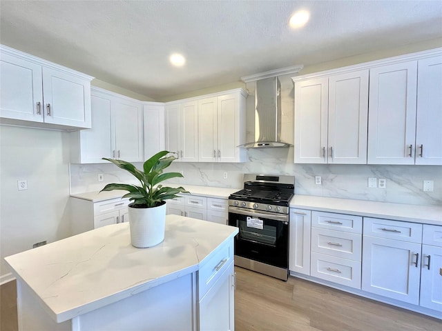 kitchen with wall chimney range hood, stainless steel gas range, white cabinetry, and tasteful backsplash