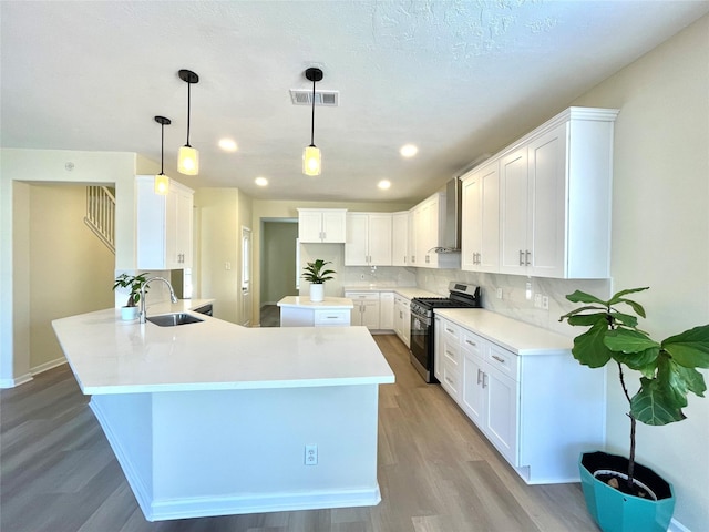 kitchen featuring a peninsula, a sink, wall chimney range hood, backsplash, and stainless steel gas stove