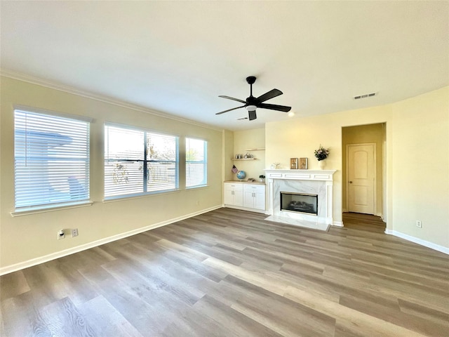 unfurnished living room with crown molding, light wood-type flooring, ceiling fan, and a fireplace