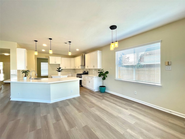 kitchen featuring sink, white cabinetry, stainless steel range, decorative light fixtures, and light wood-type flooring