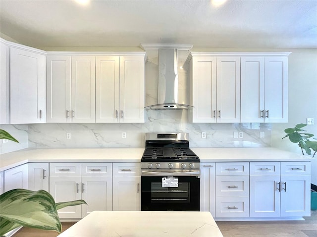 kitchen with light countertops, wall chimney range hood, stainless steel range with gas cooktop, and white cabinets