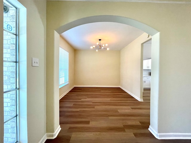 unfurnished dining area with arched walkways, baseboards, wood finished floors, and a notable chandelier