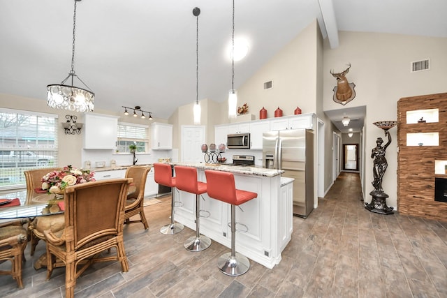 kitchen with white cabinets, appliances with stainless steel finishes, a center island, hanging light fixtures, and a notable chandelier