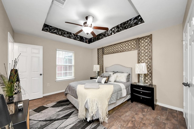 bedroom with ceiling fan, a tray ceiling, and dark hardwood / wood-style flooring