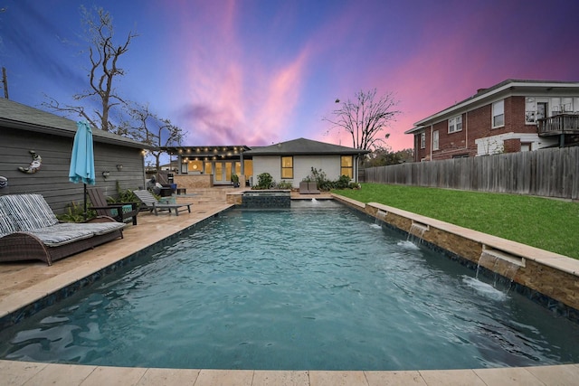 pool at dusk with pool water feature, a lawn, and a patio