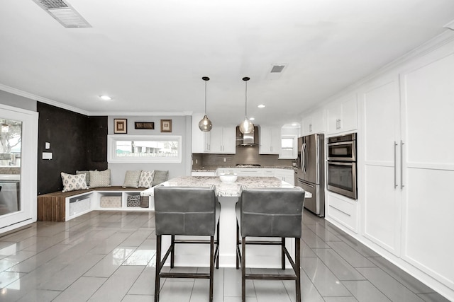 kitchen with white cabinets, a kitchen island, stainless steel appliances, hanging light fixtures, and light stone counters