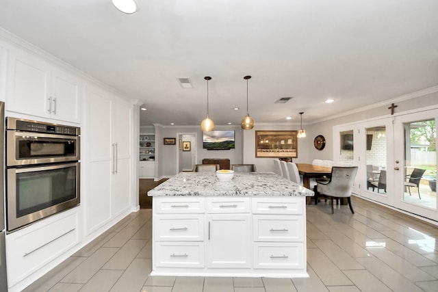 kitchen featuring light stone counters, white cabinetry, a center island, and hanging light fixtures