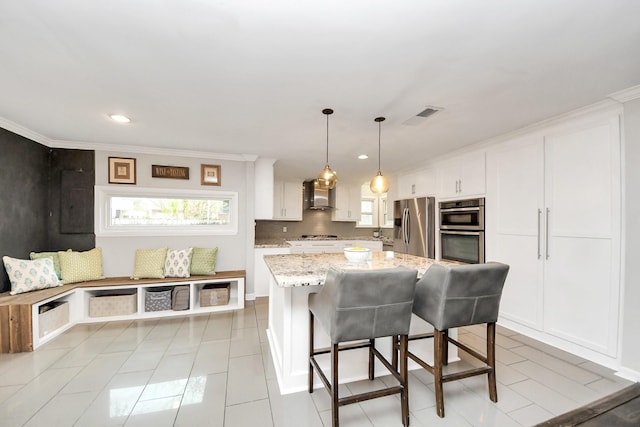 kitchen featuring appliances with stainless steel finishes, decorative light fixtures, wall chimney range hood, a kitchen island, and white cabinets