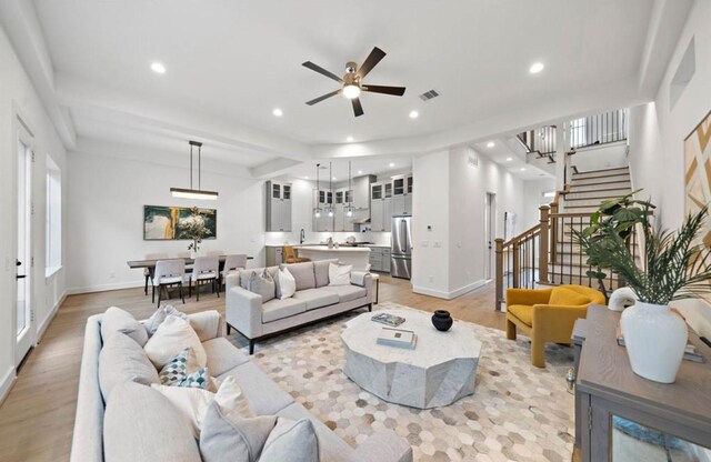 living room with ceiling fan, beamed ceiling, and light hardwood / wood-style flooring