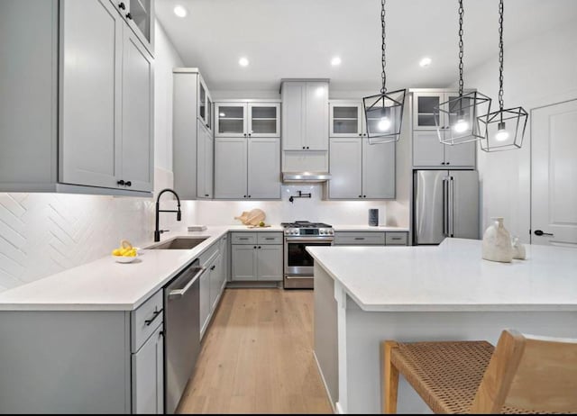 kitchen with decorative light fixtures, stainless steel appliances, light hardwood / wood-style floors, sink, and gray cabinets