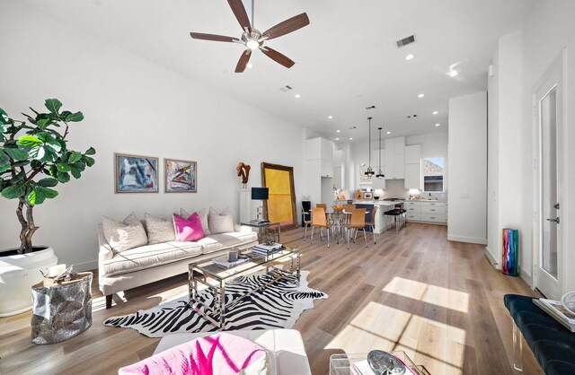 living room featuring ceiling fan, a towering ceiling, and light hardwood / wood-style flooring