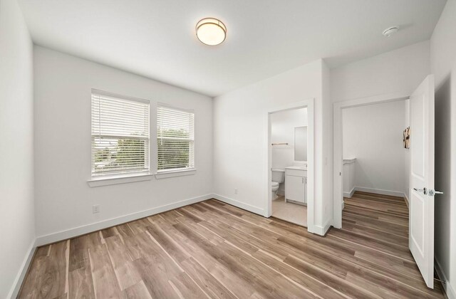 unfurnished bedroom with connected bathroom and hardwood / wood-style flooring