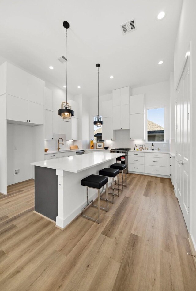 kitchen with a kitchen island, a kitchen bar, white cabinetry, light hardwood / wood-style floors, and hanging light fixtures