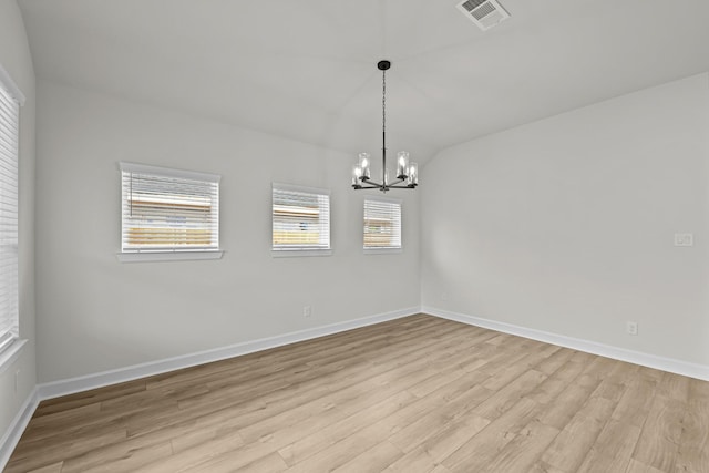 spare room with an inviting chandelier, lofted ceiling, plenty of natural light, and light hardwood / wood-style floors