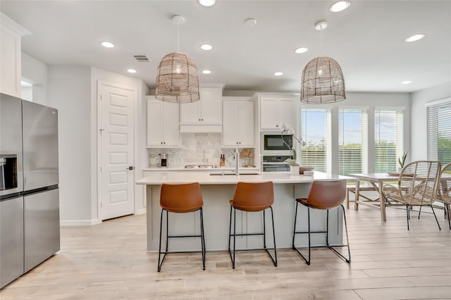 kitchen with appliances with stainless steel finishes, a kitchen island with sink, white cabinets, and decorative light fixtures