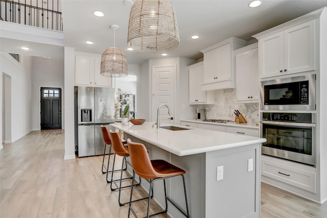 kitchen featuring appliances with stainless steel finishes, white cabinetry, decorative backsplash, sink, and a kitchen island with sink