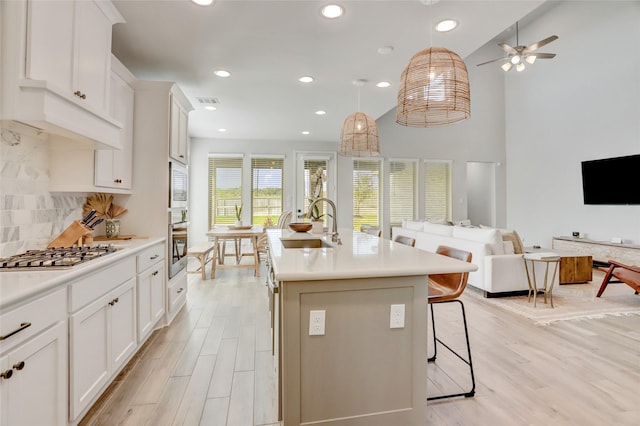 kitchen with tasteful backsplash, white cabinets, sink, and a center island with sink