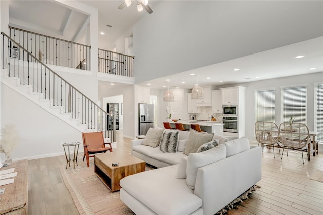 living room featuring ceiling fan, a towering ceiling, sink, and light hardwood / wood-style flooring