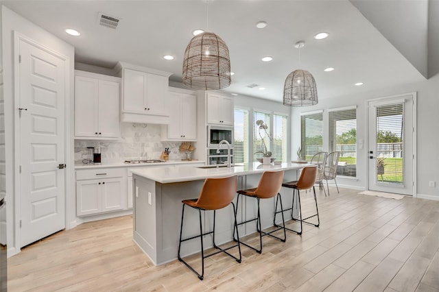 kitchen featuring decorative light fixtures, decorative backsplash, sink, white cabinetry, and an island with sink