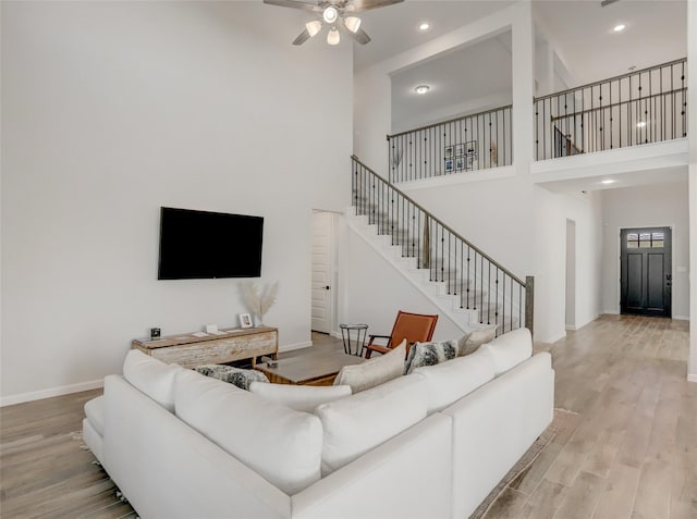 living room with light wood-type flooring, ceiling fan, and a high ceiling