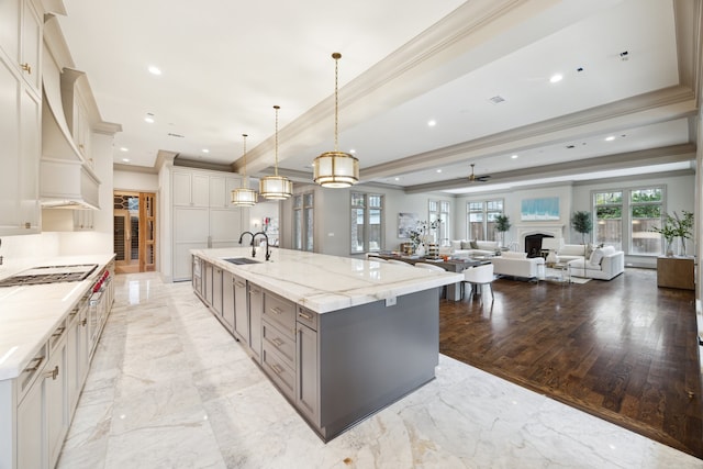 kitchen featuring sink, hanging light fixtures, a large island, light stone counters, and crown molding